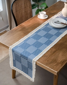Detail of blue geometric woven table runner with white handmade fringes on wooden table