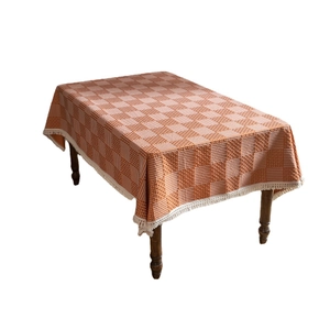 Orange-weiße Tischdecke im Karomuster mit Spitzenfransen auf einem Holztisch