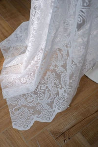 Detail of white floral lace fabric with delicate pearl beads on a wooden floor