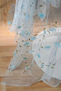 Close-up of light blue floral embroidery on sheer mesh fabric for DIY crafts