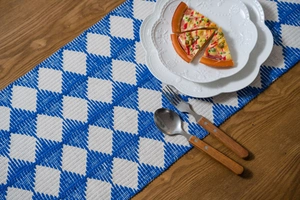 Detailed blue and white diamond woven table runner with tassel on a rustic wooden table