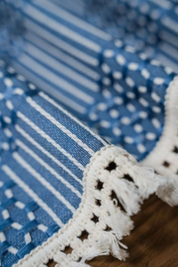 Macro shot of blue striped woven table runner featuring lace edges and tassels