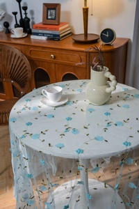 Detailed close-up of 3D light blue floral embroidery on white translucent tulle tablecloth