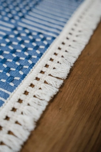 Detail of geometric blue jacquard table runner with white lace trim and fringe tassels