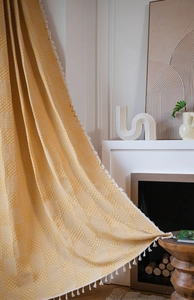 Detailed close-up of ginger yellow textured curtain with geometric patterns and white tassels