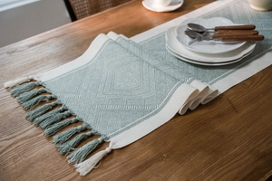 Close-up of mint green geometric woven table runner with tassel edges on wooden table