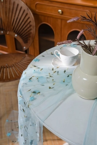 Detail view of light blue mesh tablecloth with floral embroidery and gold leaf patterns