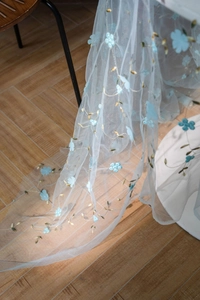 Detail showing delicate blue floral embroidery on translucent mesh fabric background