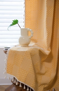 Detail of yellow woven fabric with white geometric jacquard patterns and handmade tassels