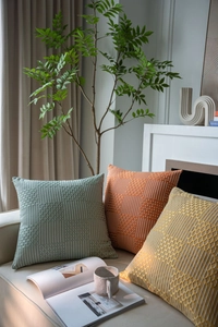 Detail of woven textured geometric pillows in sage green, orange and yellow on a sofa