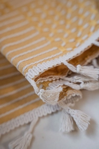 Detail of yellow and white striped textile with delicate white tassels and embroidery