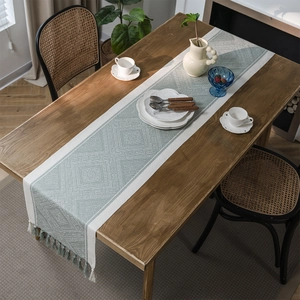Sage green and beige geometric jacquard table runner with decorative tassels on wood