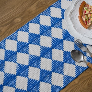 Blue and white geometric diamond woven table runner with tassels on a rustic wooden dining table