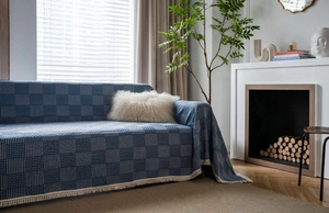 Detail shot of the geometric woven texture and cream tassels on a navy blue sofa throw