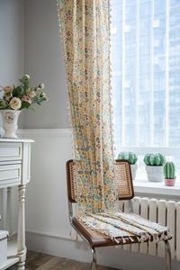 Detail of floral print linen curtain with beige tassel trim in a bright room setting
