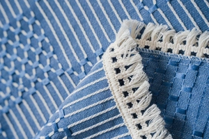 Macro detail of blue and white geometric woven fabric texture with decorative fringes