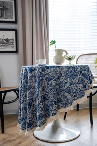 Detail of blue and white floral jacquard tablecloth with butterfly pattern and cream tassels