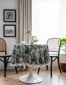 Close-up of green floral jacquard tablecloth with thick fringe on a white tulip table