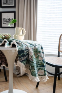 Detail of green floral jacquard tablecloth with textured weave and cream fringe tassels