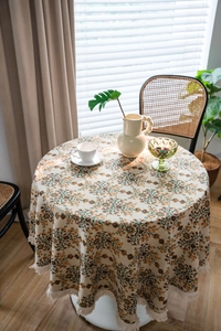 Detail showing vintage floral round tablecloth with fringe trim on a wooden table