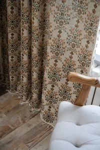 Detail of floral jacquard curtain with fringe trim in a cozy warm interior setting