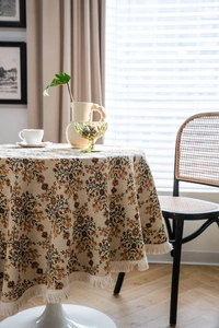 Close-up detail of vintage floral round tablecloth with cream fringe tassels on a table