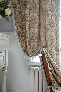 Close-up of green floral jacquard fabric curtains with elegant cream tassel fringe
