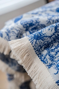 Detail der blau gemusterten Tischdecke mit cremefarbenen Fransen und fester Textur