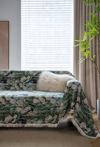 Detail of green floral jacquard sofa cover with fringe edges in a sunlit living room