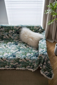 Detail of vintage green floral jacquard sofa throw with elegant cream fringe tassels
