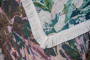 Close-up detail of green floral jacquard sofa cover with elegant white fringe edges