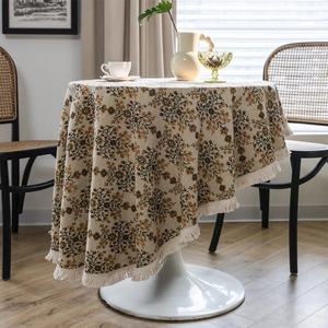 Floral round tablecloth with retro tassel trim on a wooden table in a sunlit room