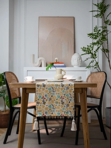 Close-up of yellow floral table runner with cotton tassels on a wooden dining table