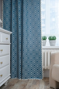 Blue and white geometric diamond pattern curtains with tassel edges in a cozy home setting