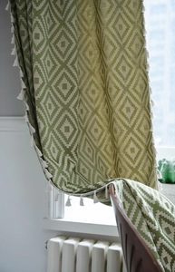 Detail of green and beige geometric diamond pattern curtain with white pom-pom fringe