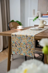 Close-up of floral print table runner with beige cotton tassels on a wooden dining table