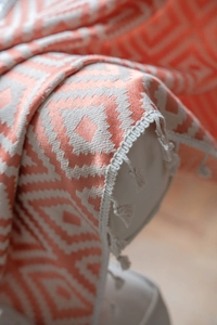 Close-up of coral orange geometric woven pattern and tassel fringe on a rustic throw blanket