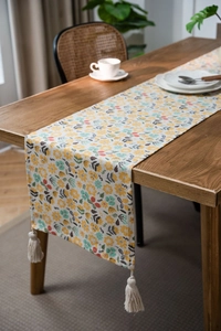 Floral print table runner with white cotton tassels on dark wood dining table