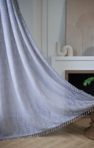 Close-up of grey crochet lace curtain featuring hollow geometric patterns and white tassels