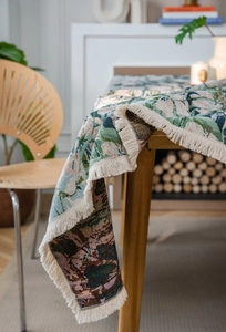 Close-up of floral jacquard tablecloth with white tassel fringe on wooden table