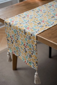 Detailed texture of floral table runner with handmade cream tassels on wooden surface