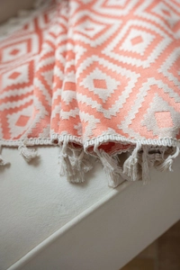 Detail of coral and cream geometric woven throw blanket with fringe tassels on sofa
