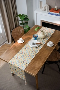 Floral print table runner with white tassels on a wooden dining table with tableware