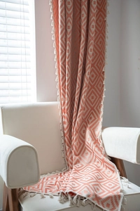 Detail of geometric diamond knit pattern on orange and cream throw blanket with tassels