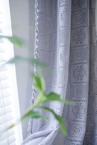 Detailed close-up of grey crochet lace curtain with geometric patterns and tassel trim edges