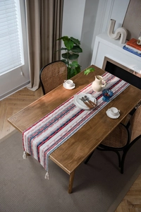 Detail of red and blue geometric table runner with white tassels on a wooden surface