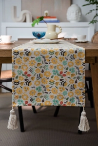 Close-up of floral print table runner with cotton fringe on rustic dark wood surface
