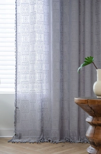 Macro view of grey crochet lace curtain with geometric square patterns and fringe tassels