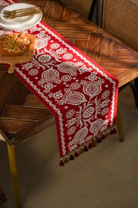 Detailed view of red festive table runner with white floral jacquard and tassel decor