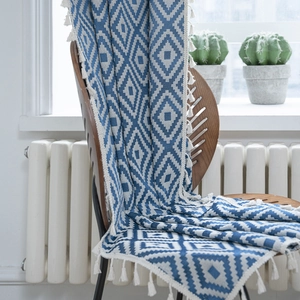 Bohemian knit blanket with blue geometric pattern and tassels on a wooden chair